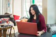 © Bojan - Smiling young woman using laptop at a cafe.