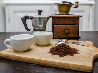 my coffee break interpretation, still life with a white two cups and two steel little spoons beside a pile of coffee powder  in the background a vintage coffee mill and an old coffee machine (moka)