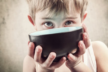 Toned Image Of A Hungry Child Holding An Empty Bowl.