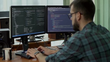a young man with a beard and glasses works behind a computer