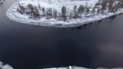 Wall Mural - Drone flying up over snow covered timber pier on wintry river with open water. Winter river bend is in swamp. Karelia, Russia
