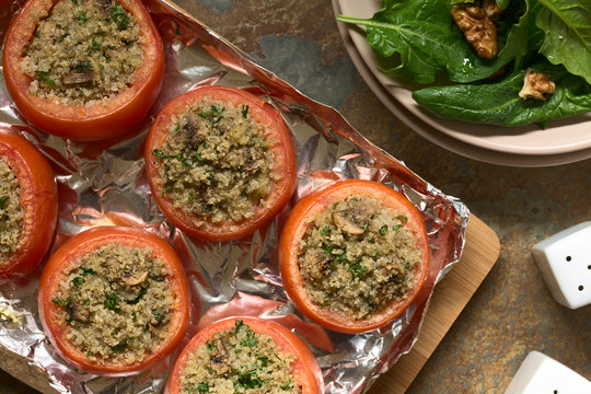 Vegetarian baked tomato stuffed with quinoa, mushroom and parsley with spinach and walnut salad on the side, photographed overhead  on slate with natural light