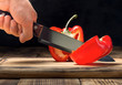 Man's hand with a kitchen knife cuts red pepper