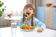 © Africa Studio - Small girl eating vegetables in kitchen