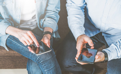 Close-up of smartphones in hands of young man and woman,dressed in jeans and shirts.Couple using digital gadgets for online shopping, chatting, blogging, surfing internet,sms.Freelancers working home.