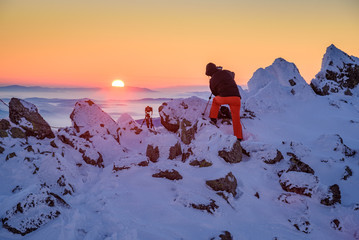 Wall Mural - Photographer in winter clothing at work - capturing a beautiful winter landscape on a mountain top