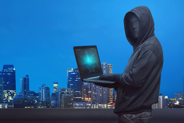 Wall Mural - Hooded hacker with anonymous mask typing on laptop