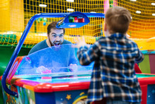 Father And Son Playing Air Hockey Game At Amusement Park