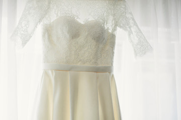 Lace bridal gown hangs before the window