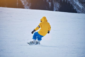 Wall Mural - Snowboarder in bright yellow jacket and blue pants makes backside carved turn on snow slope at sunny winer day in mountain ski resort