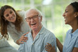 © Erickson Stock - Portrait of a laughing senior man being comforted by a female nurse and his adult daughter while wearing pajamas.