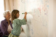 © Erickson Stock - Mature woman happily watches her young granddaughter write on a bedroom mural wall with a felt pen.