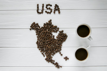 Wall Mural - Map of the USA made of roasted coffee beans laying on white wooden textured background with two cups of coffee. Space for text