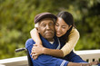 © Erickson Stock - Young woman leans over and embraces her grandfather sitting in a wheelchair as they pose for a portrait on a porch.