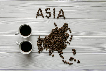 Wall Mural - Map of the Asia made of roasted coffee beans laying on white wooden textured background with two cups of coffee