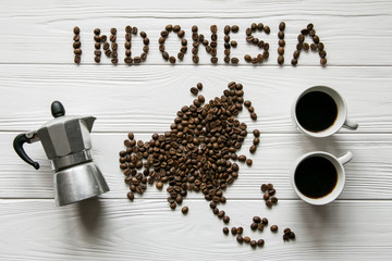 Map of the Indonesia made of roasted coffee beans laying on white wooden textured background with two cups of coffee and coffee maker