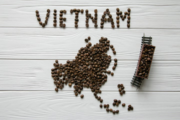  Map of the Vietnam made of roasted coffee beans laying on white wooden textured background with toy train