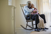 Senior Man Sitting In A Rocking Chair With His Grandson.