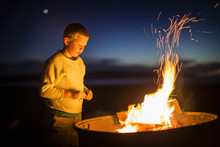 Boy Looking At Glowing Campfire At The Beach