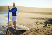 Portrait Of A Smiling Mature Woman Standing With Her Paddleboard.