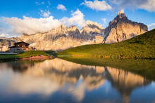 The Pale Di San Martino Peaks (Italian Dolomites) Reflected In The Water At Sunset, With An Alpine Chalet On Background.