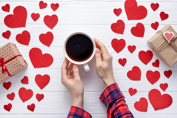 Wall Mural - Woman hands in checkered shirt holding on to a cup of coffee on the white wooden table with hearts and gifts. Romantic background to Valentine's Day, Dating, couples in love. Flat lay.