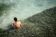© Erickson Stock - Rear view of woman sitting in seaweed in shallows of clear ocean