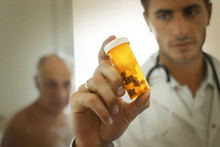 Doctor Holding Up A Bottle Of Pills With A Worried Look On His Face.
