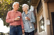© Erickson Stock - Smiling senior couple walk down the street drinking coffee and looking at each other.