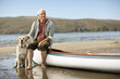 © Erickson Stock - Happy senior man sitting on the edge of a canoe with his dog.
