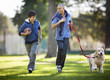 © Erickson Stock - Smiling mid adult man and his son having fun jogging together in the park with their dog.