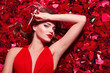 © EkaterinaJurkova - Valentine's Day. Loving girl. The girl in a red dress lying on the floor in the petals of red roses. Background of red rose petals. Red lipstick on the lips from the beautiful girl.