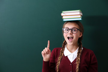 Poster - Teenage girl with books on her head standing near green school blackboard