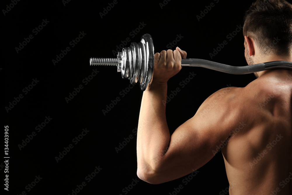 Sporty man doing exercises with barbell on black background