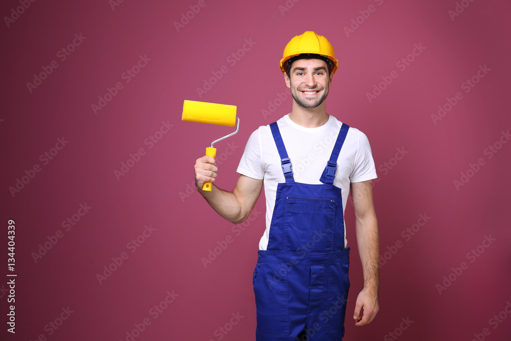 Handsome young worker with paint roller on color background