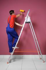 Canvas Print - Young decorator painting wall while standing on ladder