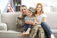 Soldier In Camouflage And His Family Sitting On Sofa At Home