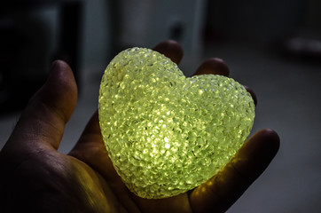 Valentine`s day concept. Multicolor lighting Heart in the man hand on blurred dark background