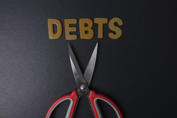 Wall Mural - Scissors and word of DEBTS on black background. Business concept