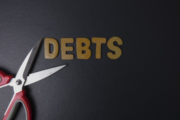 Wall Mural - Scissors and word of DEBTS on black background. Business concept