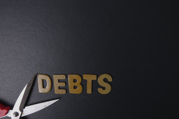 Wall Mural - Scissors and word of DEBTS on black background. Business concept