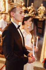 Happy bride & groom in church with candles & crowns