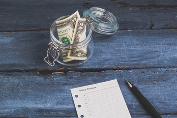 two dollars in the jar and diary planner on a blue wooden backgr