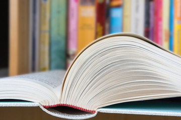 An open book in foreground with a blurred colorful library in background