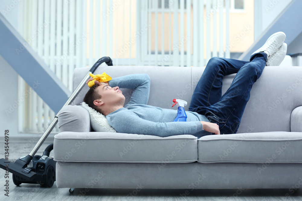 Young tired man lying on sofa after cleaning