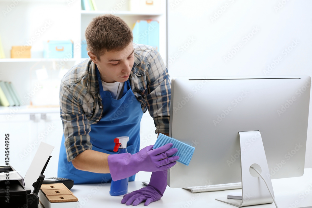 Young man cleaning computer monitor in office