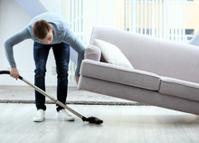 Young man with vacuum cleaner cleaning floor at home