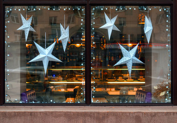 Stars of paper in the window of a cafe. Christmas decoration storefront with garland lights and paper stars in european city street at winter seasonal holidays