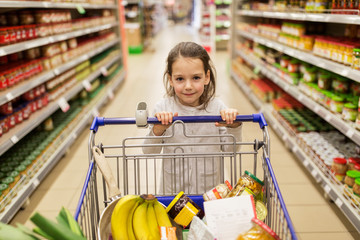 Wall Mural - girl with food in shopping cart at grocery store