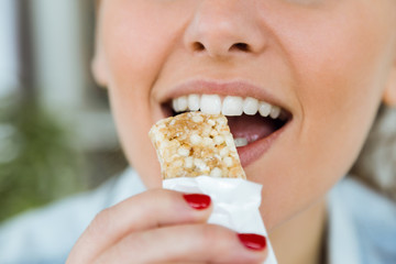 Beautiful young woman eating muesli snack at home.